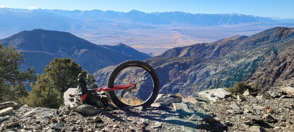 A mountain unicycle is propped on the edge of a cliff in a high desert landscape. In the foreground and background are many broken up sharp rocks.